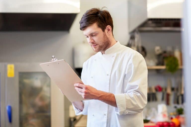 Chef in Kitchen reviewing Clipboard with information