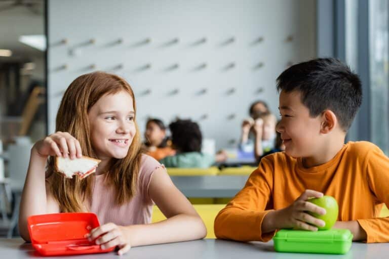 Two children in school cafeteria eating lunch and smiling