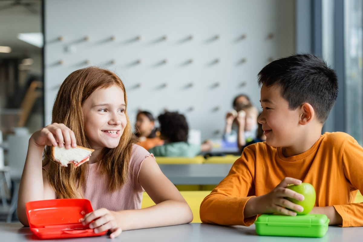 Two children in school cafeteria eating lunch and smiling