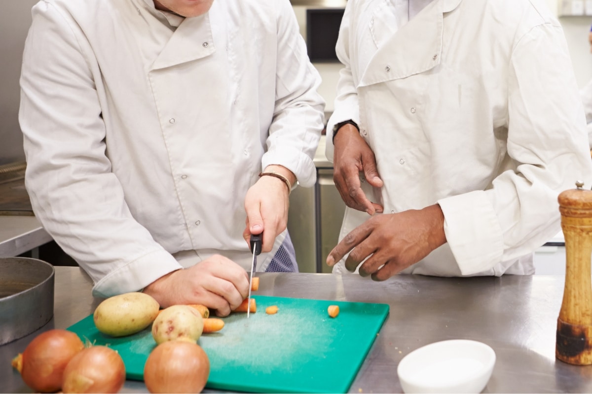 Two chefs in white coats stand over a cutting board