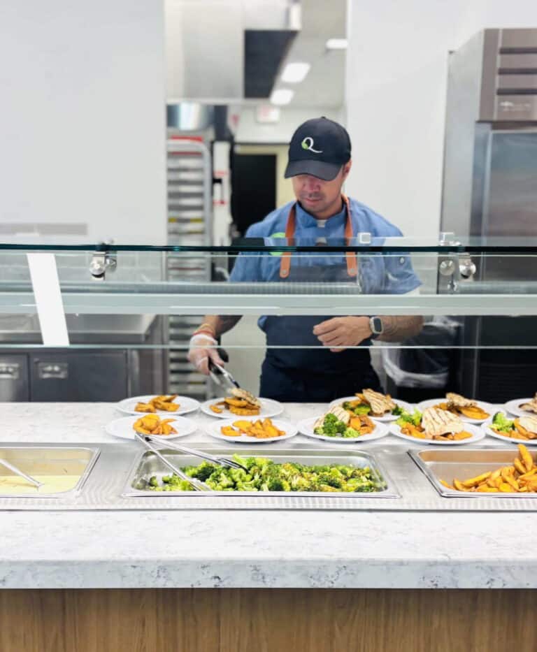 A man in a blue shirt prepares food at a buffet, arranging dishes and ingredients for guests.