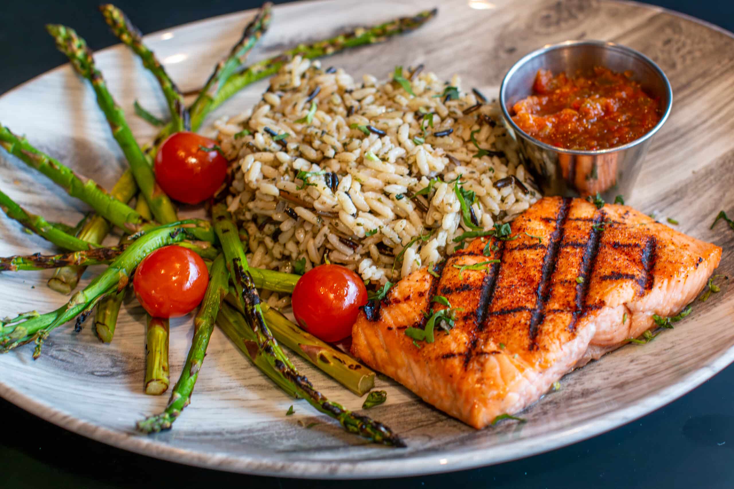 A plate filled with grilled salmon, rice, asparagus, and tomatoes.