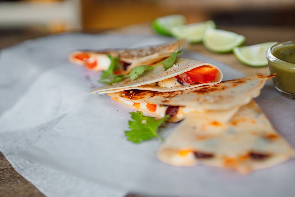 Close-up of a mouthwatering quesadilla with fresh cilantro and lime on wax paper.