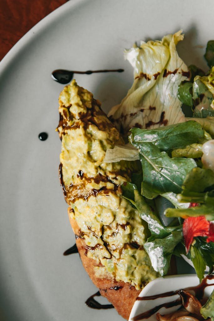 Close-up of a tasty avocado toast served with a fresh mixed salad, drizzled with balsamic glaze.