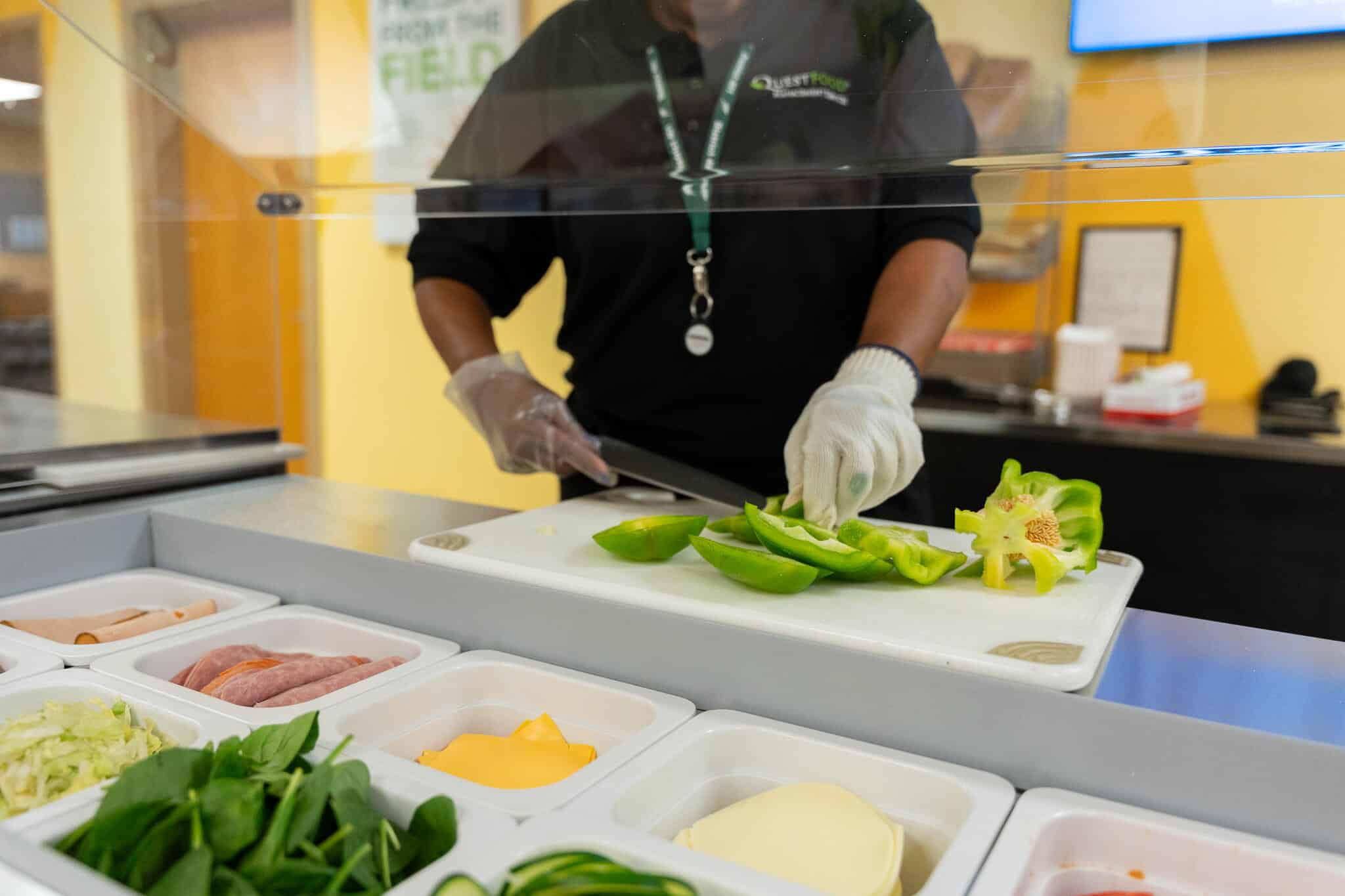 A woman in a kitchen rinsing fresh vegetables under running water at the sink.