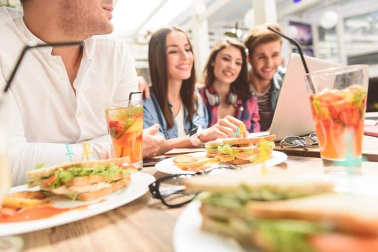 A group of people gathered around a table enjoying sandwiches and engaging in conversation.