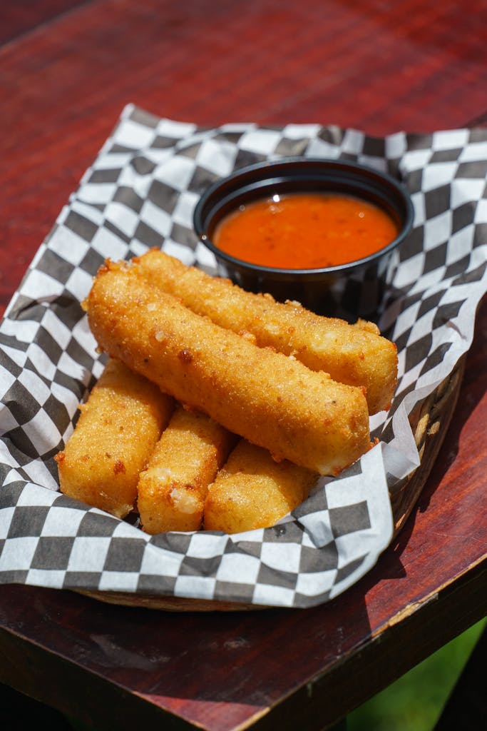 Golden fried mozzarella sticks served with marinara sauce on a checkered paper.