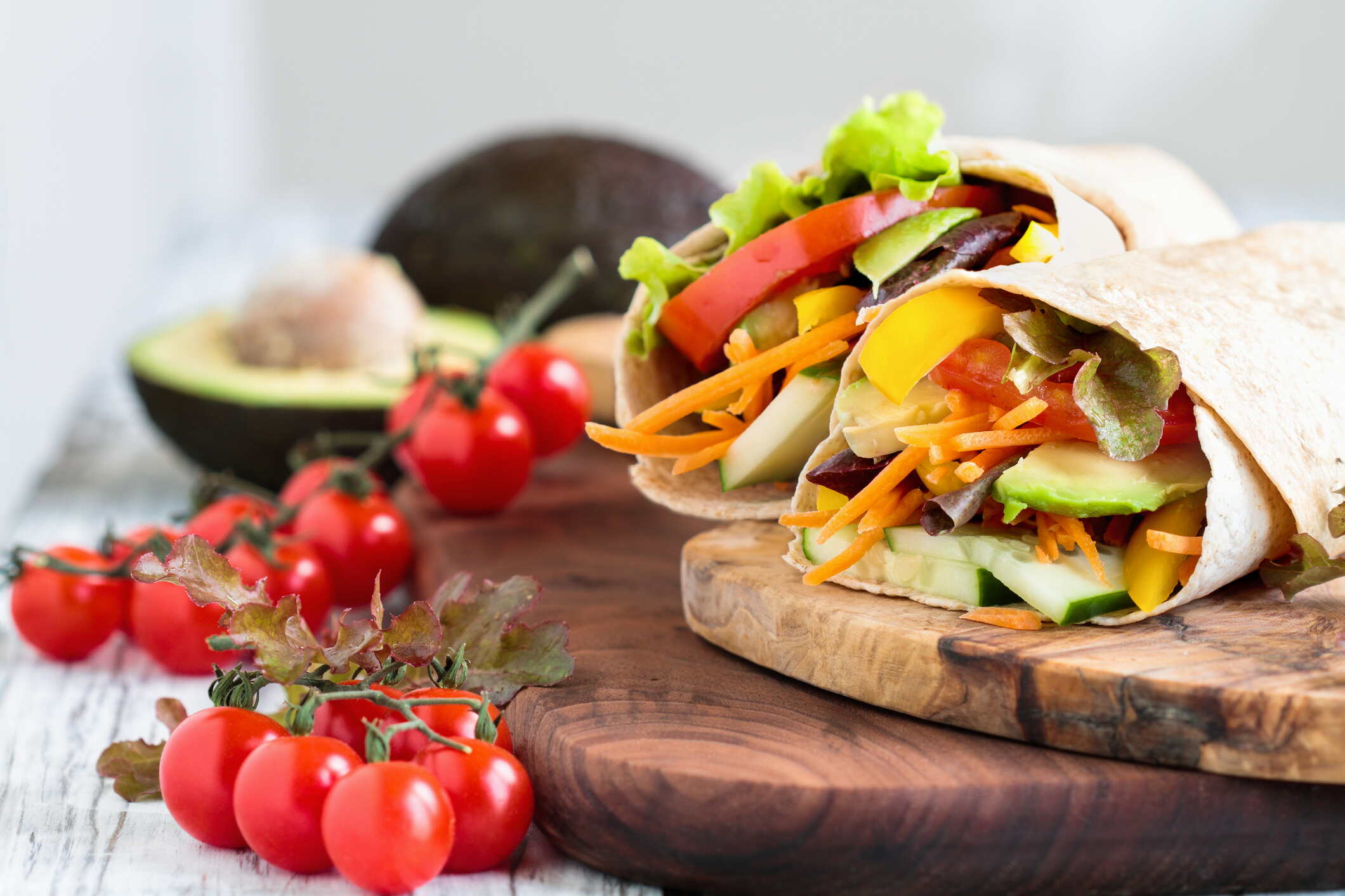 A healthy lunch or dinner of a vegan / vegetarian wrap made with argula lettuce, sliced tomatoes, cucumbers, avocado, bell peppers and carrots. Selective focus on sandwich in front.