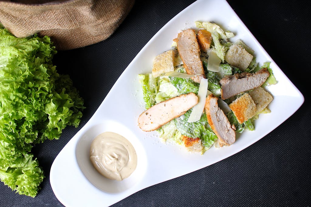 Top view of a chicken Caesar salad on a white plate with Caesar dressing.
