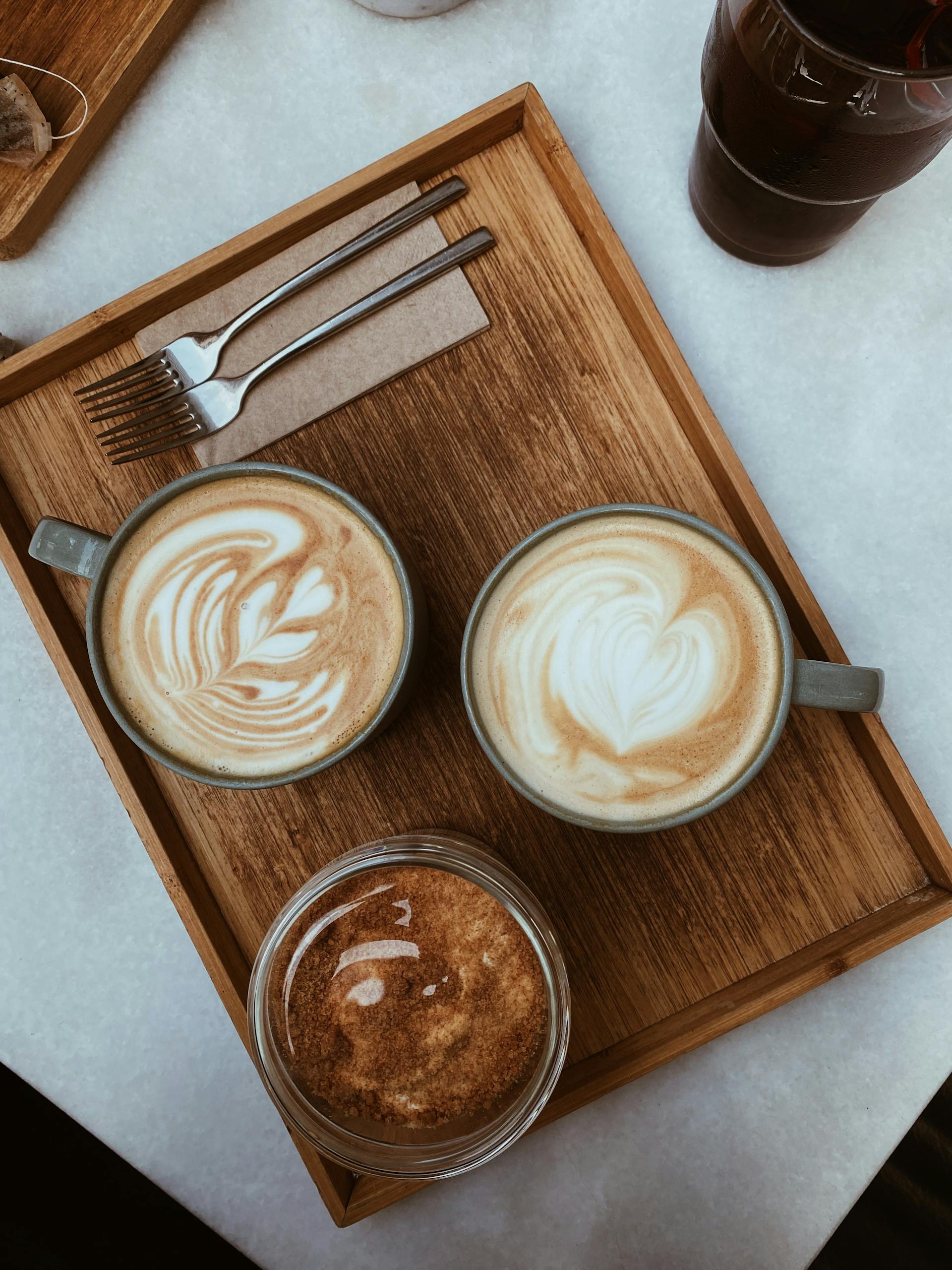Top view of cappuccinos with latte art served on a wooden tray, setting a cozy café vibe.